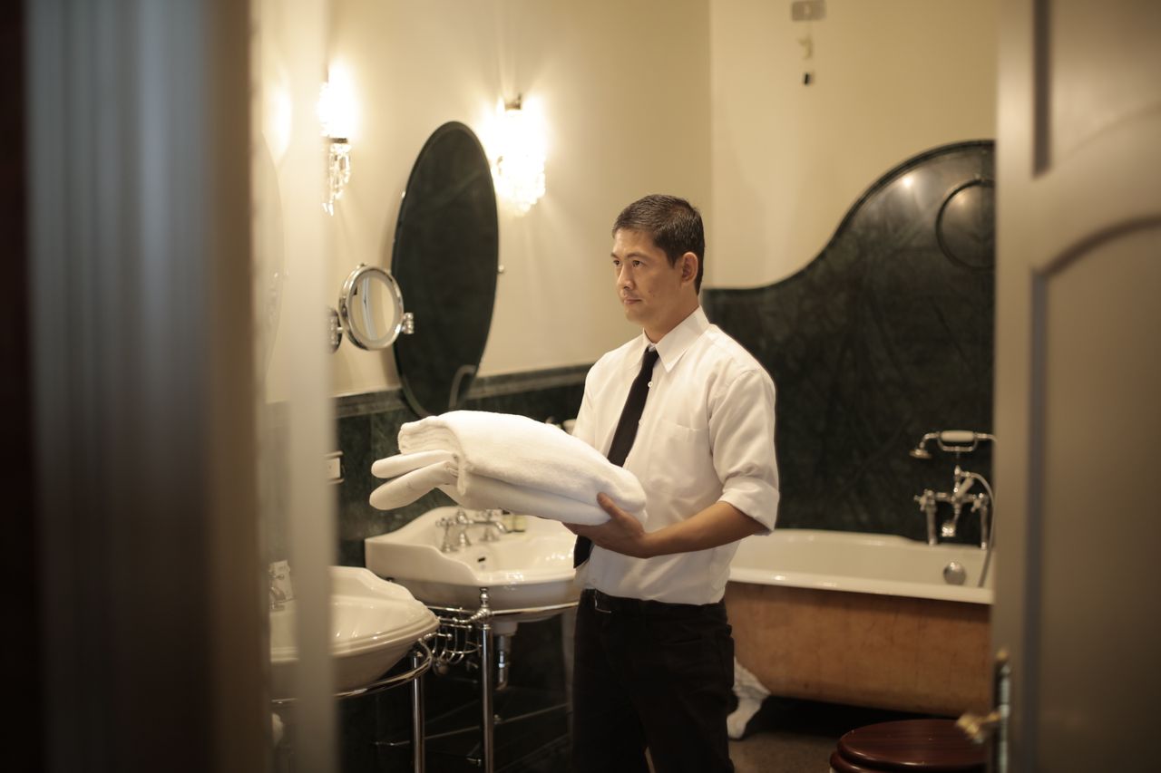 who-we-are Side view of young male employee holding stack of white towels while standing in bathroom of luxury hotel